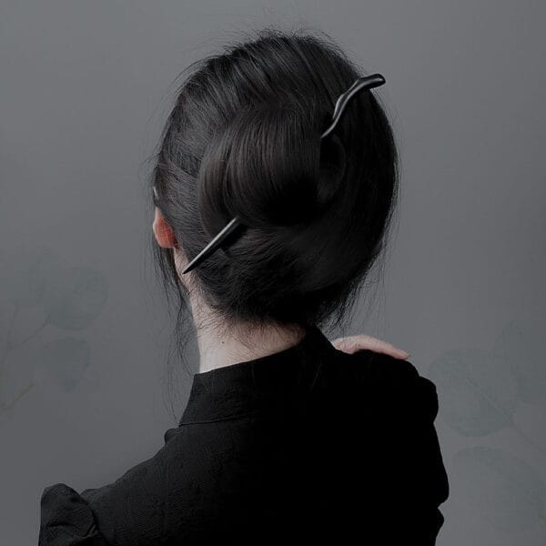 Black wooden hair stick in a woman's dark bun. Elegant hair accessory.