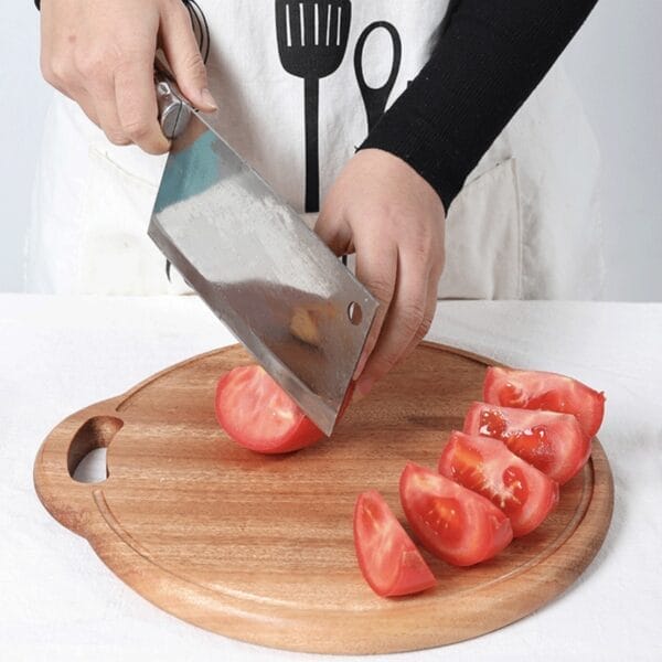 Round wooden cutting board with handle, ideal for chopping vegetables like tomatoes using a cleaver.