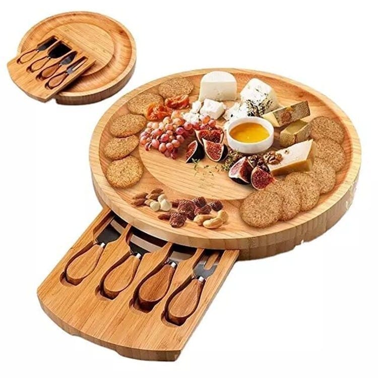 Round bamboo cheese board with built-in cheese knives and assorted cheeses, crackers, and fruits.