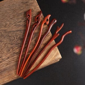 Six wooden hair sticks with ornate carvings on a wooden surface.