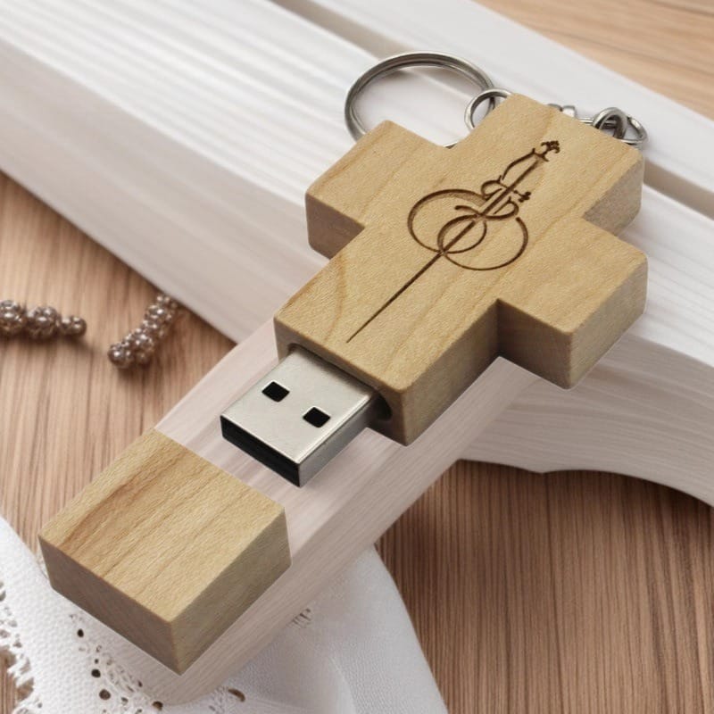 Wooden cross USB drive with engraved sword and design, displayed on a light wooden surface.