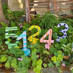 Colorful wooden numbers 1, 2, 3, 4, 5 displayed among green clover plants.