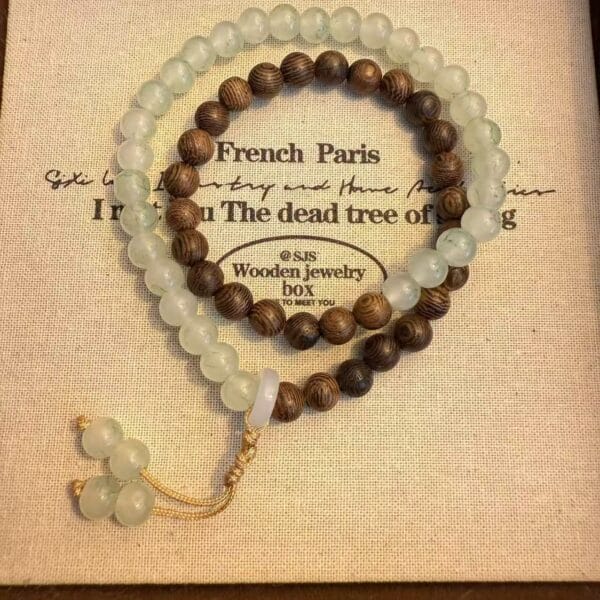 Beaded bracelets: light green & brown wood beads, on a beige box. Mala beads, jewelry.