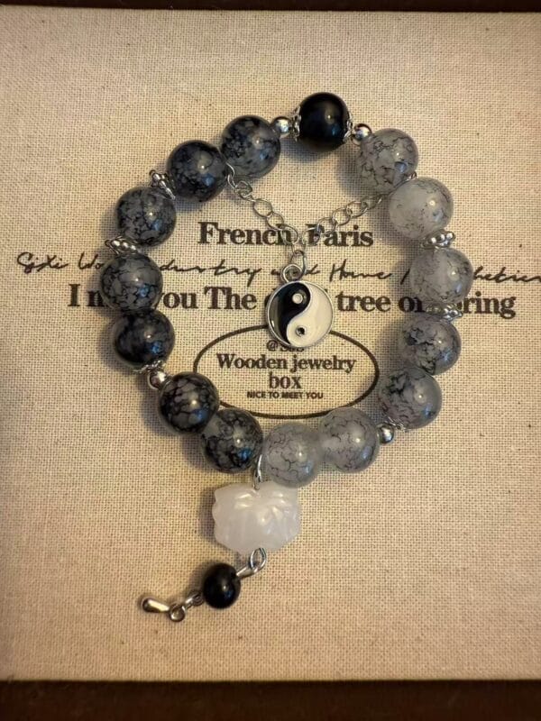 Beaded bracelet with black and gray beads, a yin yang charm, and a white flower pendant.