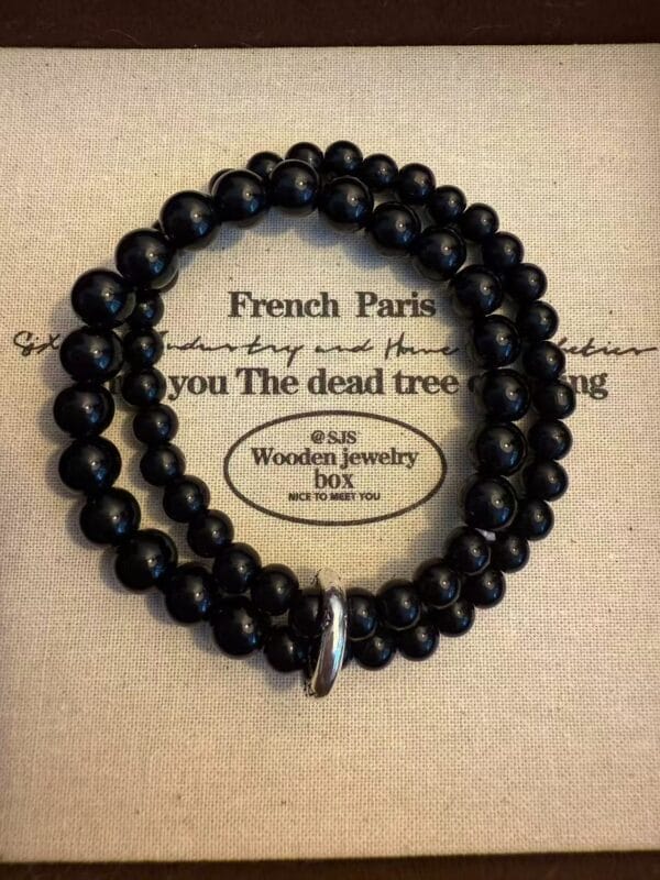 Black bead bracelet: Two-strand design with silver clasp. Stylish jewelry on patterned surface.