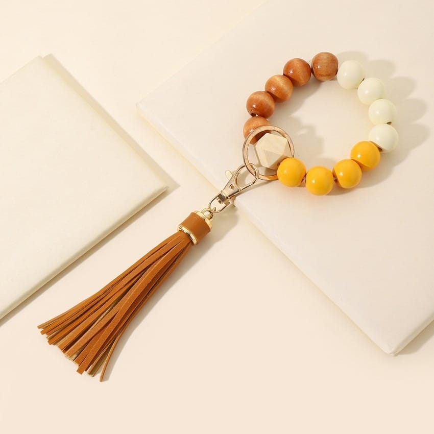 Beaded bracelet keychain with wood, white, and yellow beads and a brown leather tassel