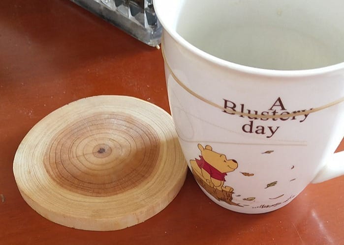 Wooden coaster next to a Winnie the Pooh mug, perfect for protecting surfaces from hot drinks.
