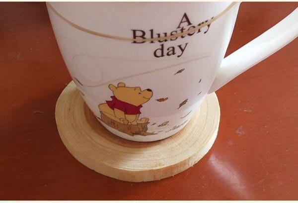 Mug with Winnie the Pooh design on a round wooden coaster.