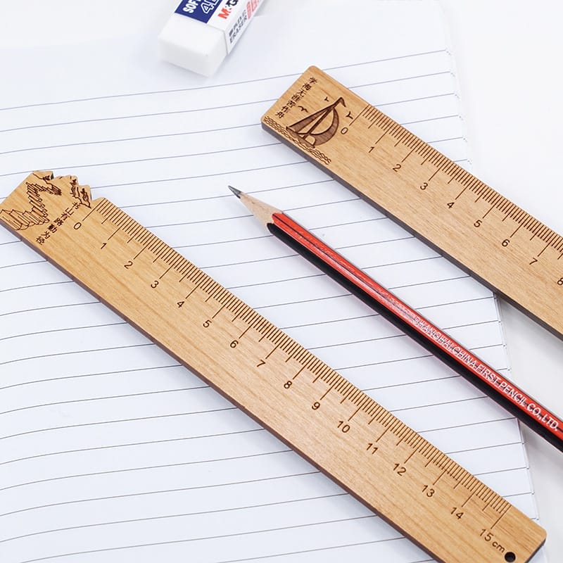 Wooden rulers, pencil, and eraser on lined paper. One ruler reads: "First Pencil Co., LTD.