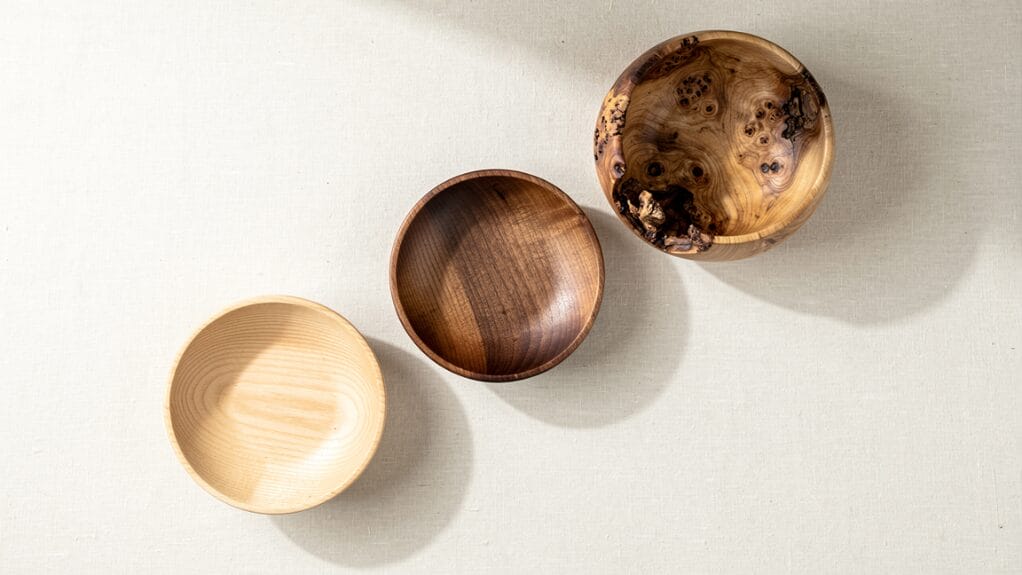Three wooden bowls of various wood types and finishes displayed on a textured surface