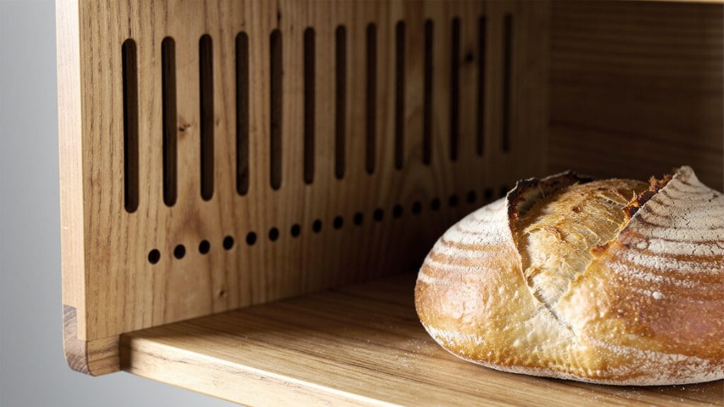 Fresh sourdough loaf in a wooden bread box with ventilation slots.