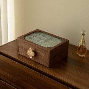 Elegant wooden jewelry box with textured glass top and clover-shaped drawer pull on a wood dresser.