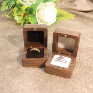 Two wooden ring boxes, one with a gold ring, the other with a silver ring, on a textured surface with flowers.