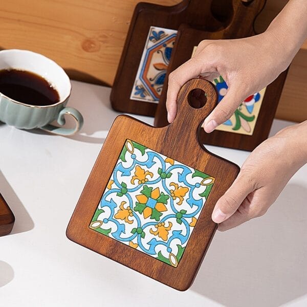 Hand holding wooden serving board with decorative tile insert.