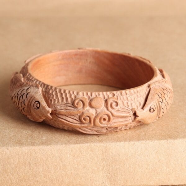 Carved wooden bangle featuring a detailed fish design, showcasing craftsmanship and natural beauty.