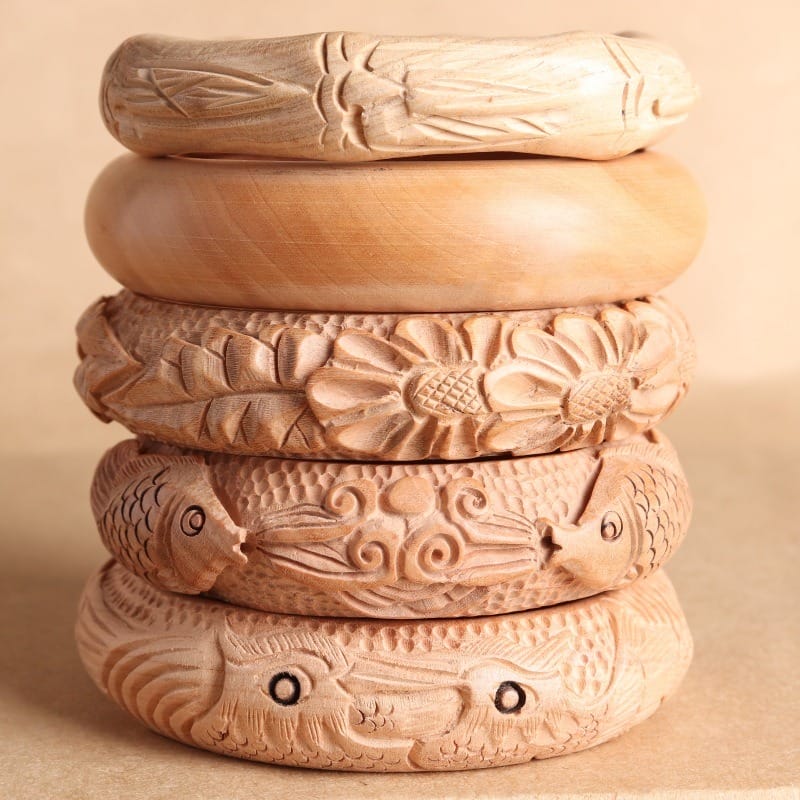 Stack of five intricately carved wooden bangles featuring floral and animal designs.