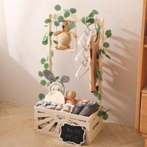 Baby clothes rack with clothes, shoes, and stuffed animals in a wooden crate, decorated with greenery.