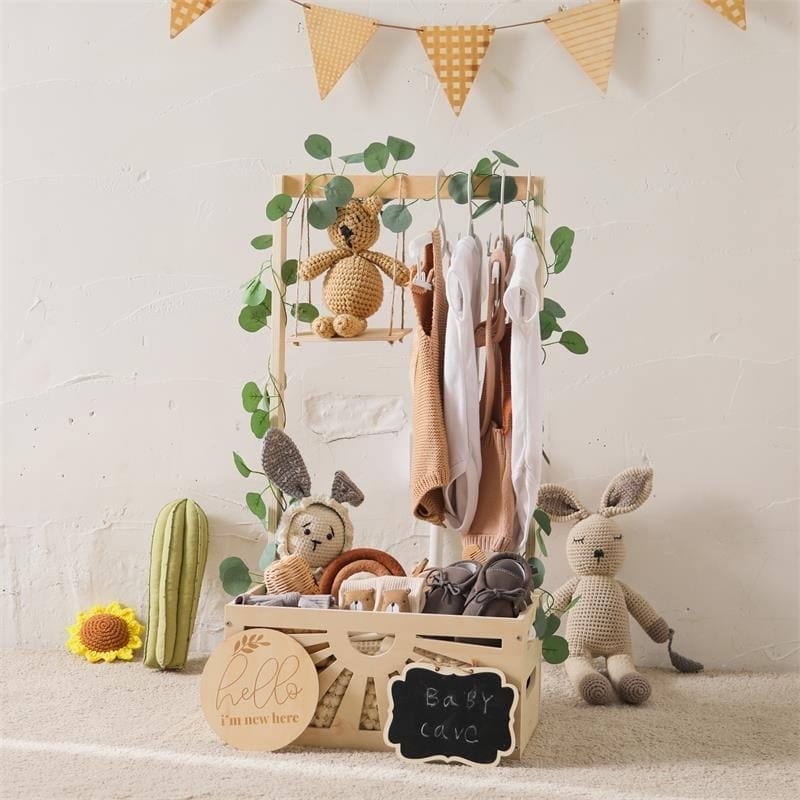 Baby clothes on wooden rack with stuffed animals and "Baby Cave" wooden crate. Cute nursery decor.