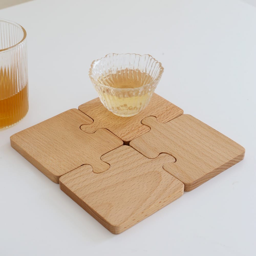 Wooden puzzle coasters forming a square, topped with a glass bowl and a drink alongside.