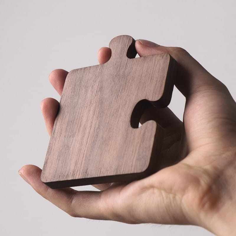 Hand holding a dark wooden jigsaw puzzle piece, showcasing its grain and shape.