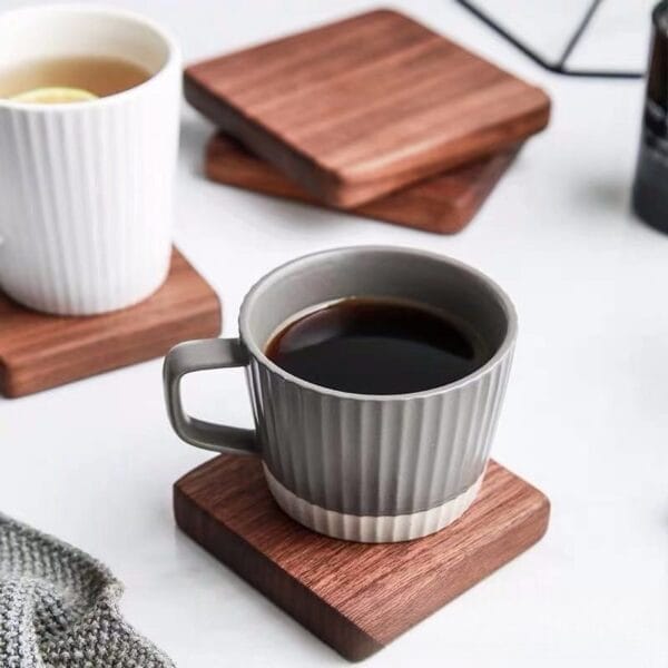 Gray mug on square wood coaster; tea cup and coasters in background. Minimalist design.