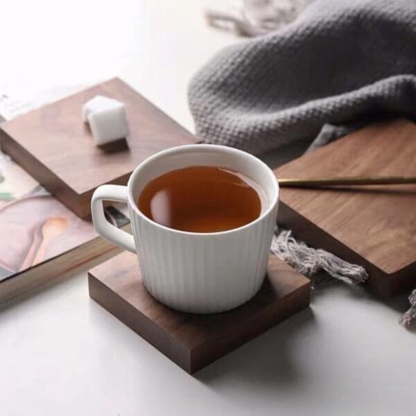 White ribbed mug with tea on wood coaster. Sugar cubes & cozy blanket in background.