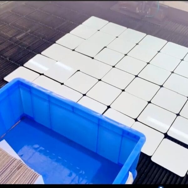 AUTO-DRAFT: White square tiles arranged in a grid pattern, next to a blue plastic bin filled with tiles