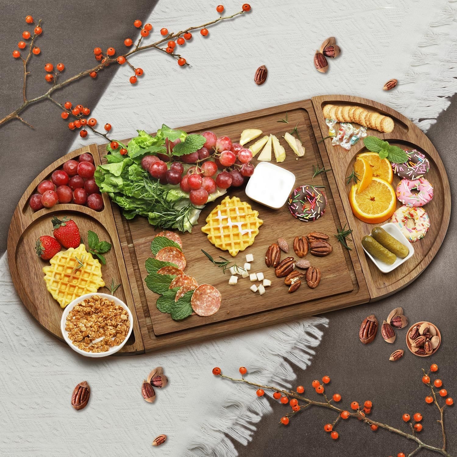 Wooden charcuterie board with grapes, waffles, cheese, salami, nuts, pickles, and donuts.