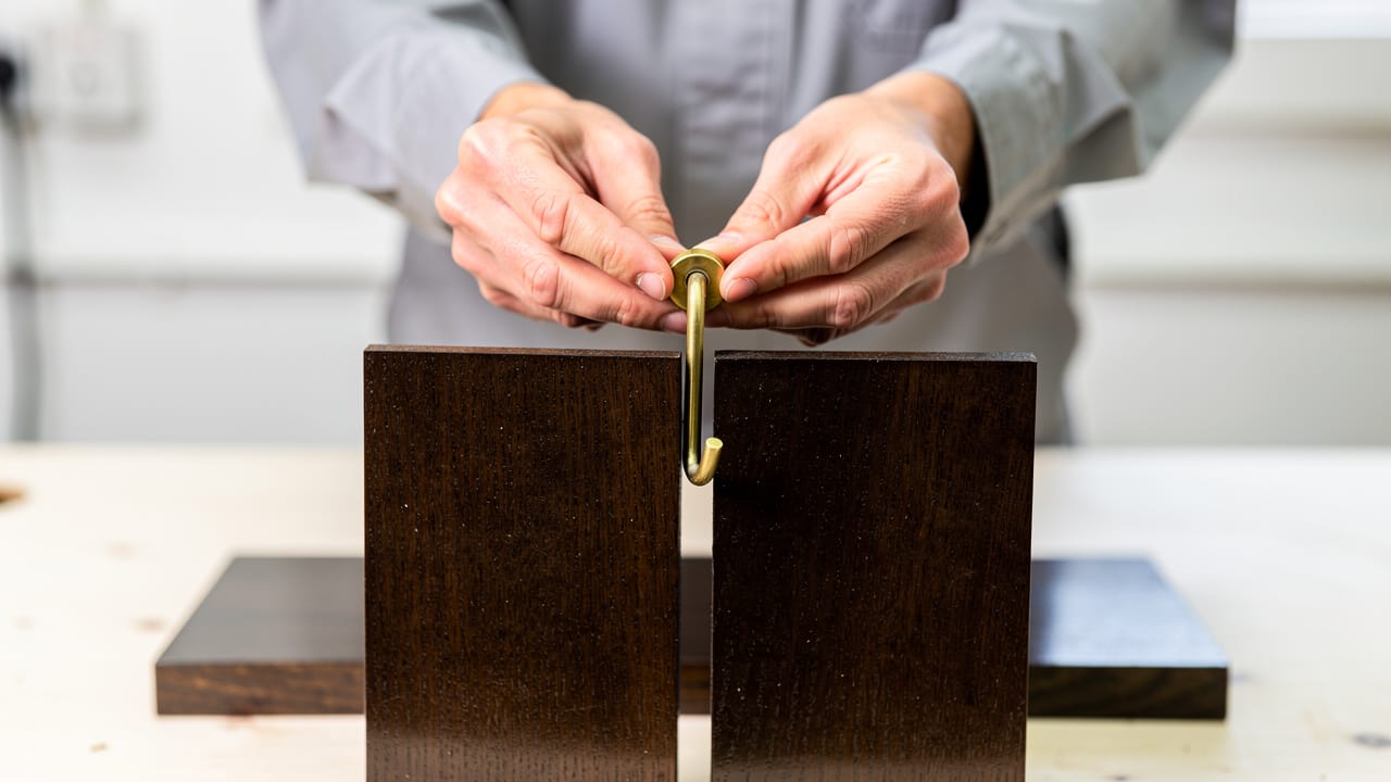 Hands attaching a brass hook to a wooden key holder design.