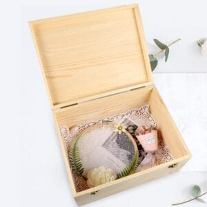 Open wooden box revealing gifts inside, including an embroidered hoop and a small floral bouquet.