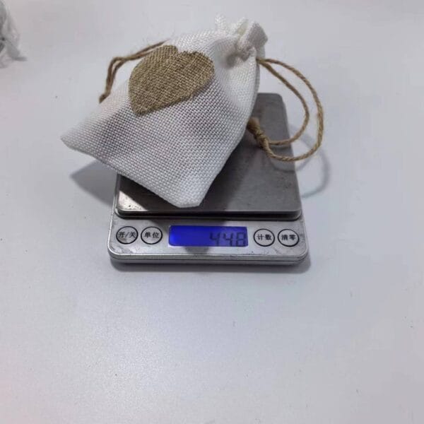 AUTO-DRAFT: Small white burlap bag with brown heart, weighing 44.8 on a scale