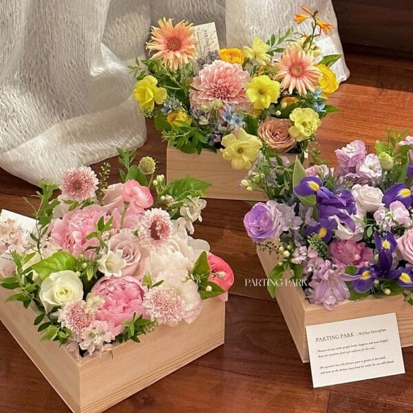 Mini Wooden Boxes Wholesale: Three wooden boxes filled with vibrant floral arrangements in pink, yellow, and purple hues.