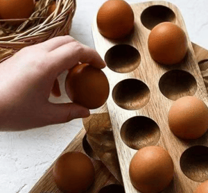 Wooden egg holder with brown eggs being placed in the slots. Eco-friendly kitchen egg storage tray.