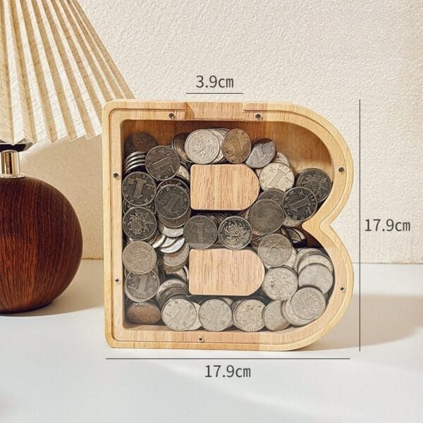 Letter "B" coin bank: Wooden piggy bank shaped like the letter B, filled with coins and labeled with dimensions