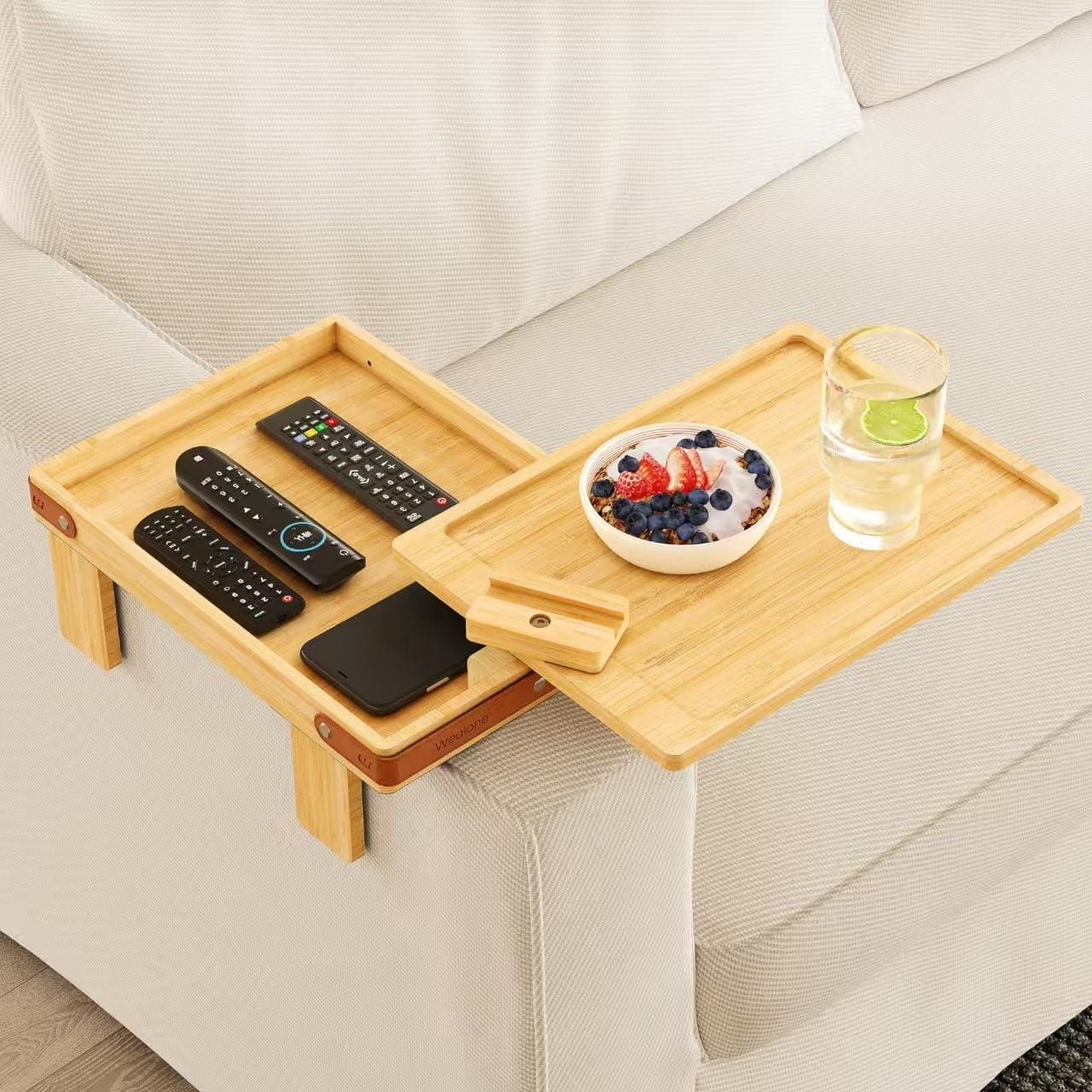 Sofa arm tray table holding remotes, phone, drink, and fruit bowl, offering convenient couch-side access