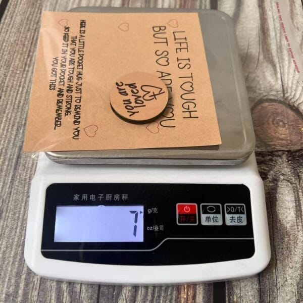 Pocket Hug: Engraved mini wooden token with a supportive message, displayed on a scale with accompanying card.