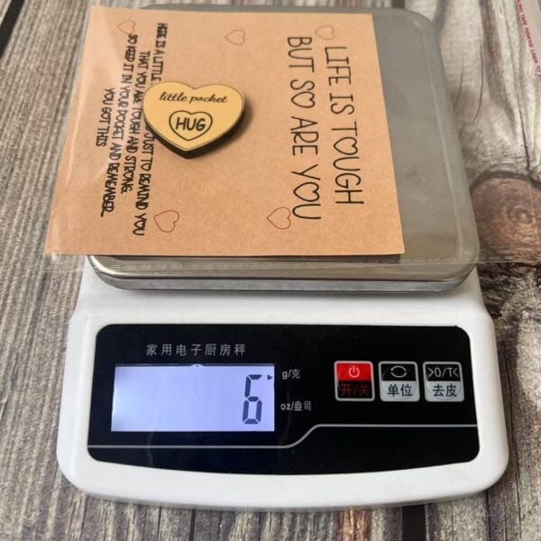 Pocket Hug: Wooden heart token on a scale, with a card that offers encouragement and support.