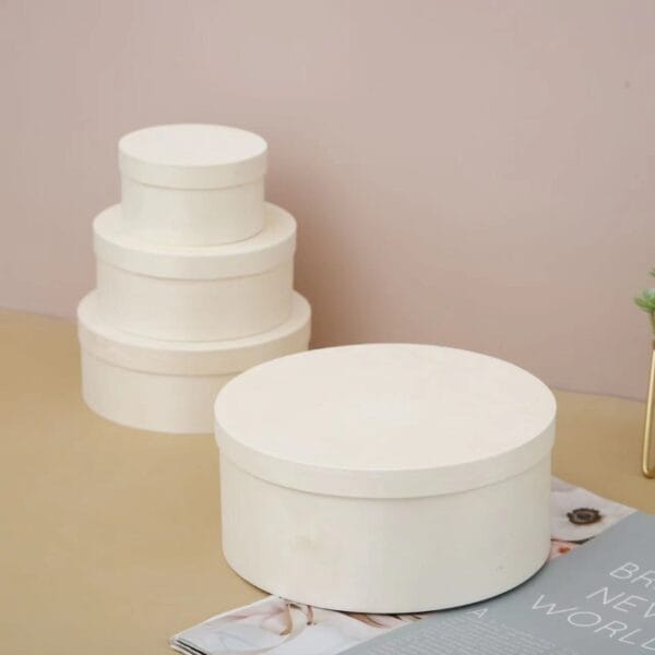 Round Wooden Boxes Wholesale : Stack of three white round boxes and a single round box on a beige surface