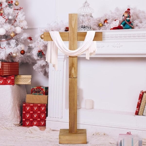 Wooden cross draped with white cloth, set in a decorated room with gifts and a white Christmas tree.