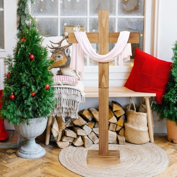 Wooden cross draped with white cloth, displayed with Christmas trees and firewood.