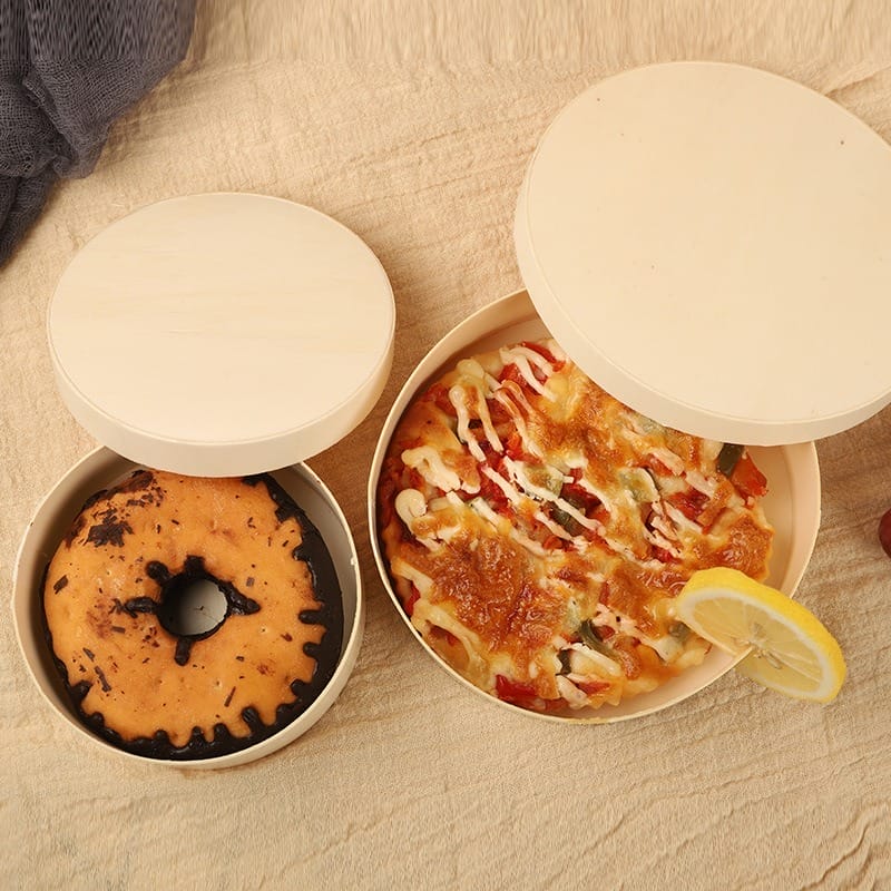 Donut and pizza in round wooden boxes with lids, shown on a beige cloth background.