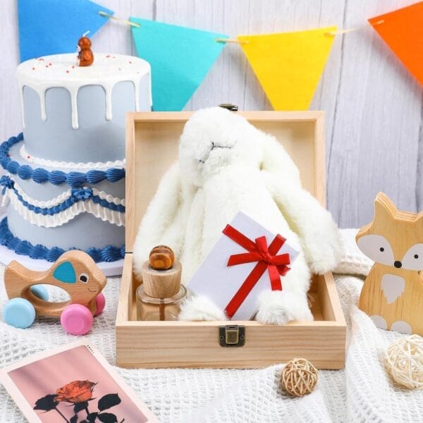 White stuffed bunny in wooden box with gift card. Birthday cake and wooden toys in background.