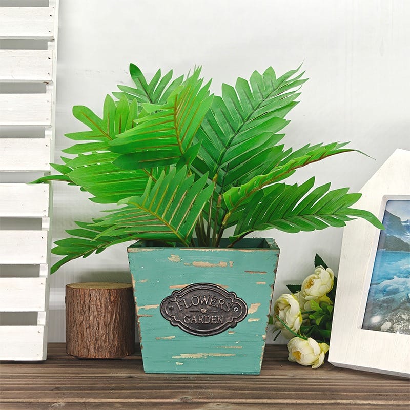 Potted plant with green leaves in a distressed blue "Flowers Garden" pot.