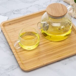 Wooden serving tray with glass teapot and cup filled with tea. Small bamboo snack tray.
