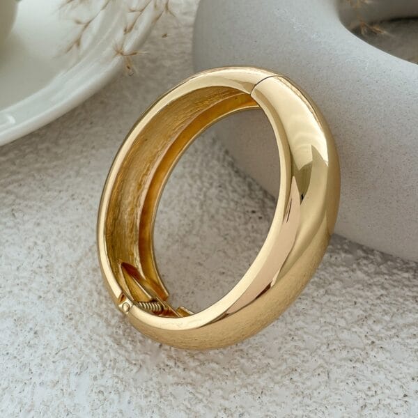 Gold bangle bracelet with a hinged closure, part of a vintage geometric wooden bangle set.