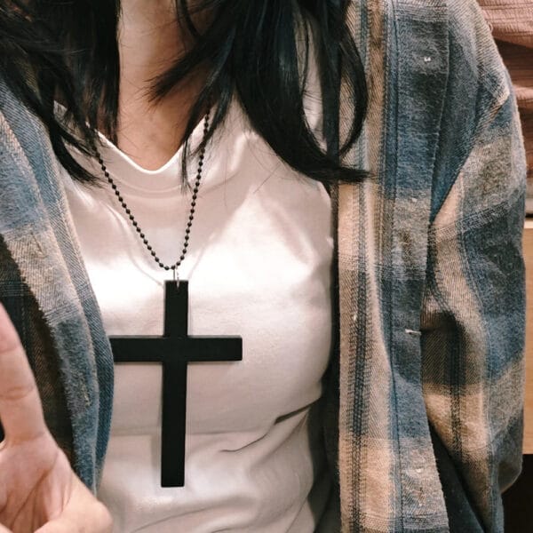 Woman in flannel wearing a white t-shirt and a large black cross necklace.