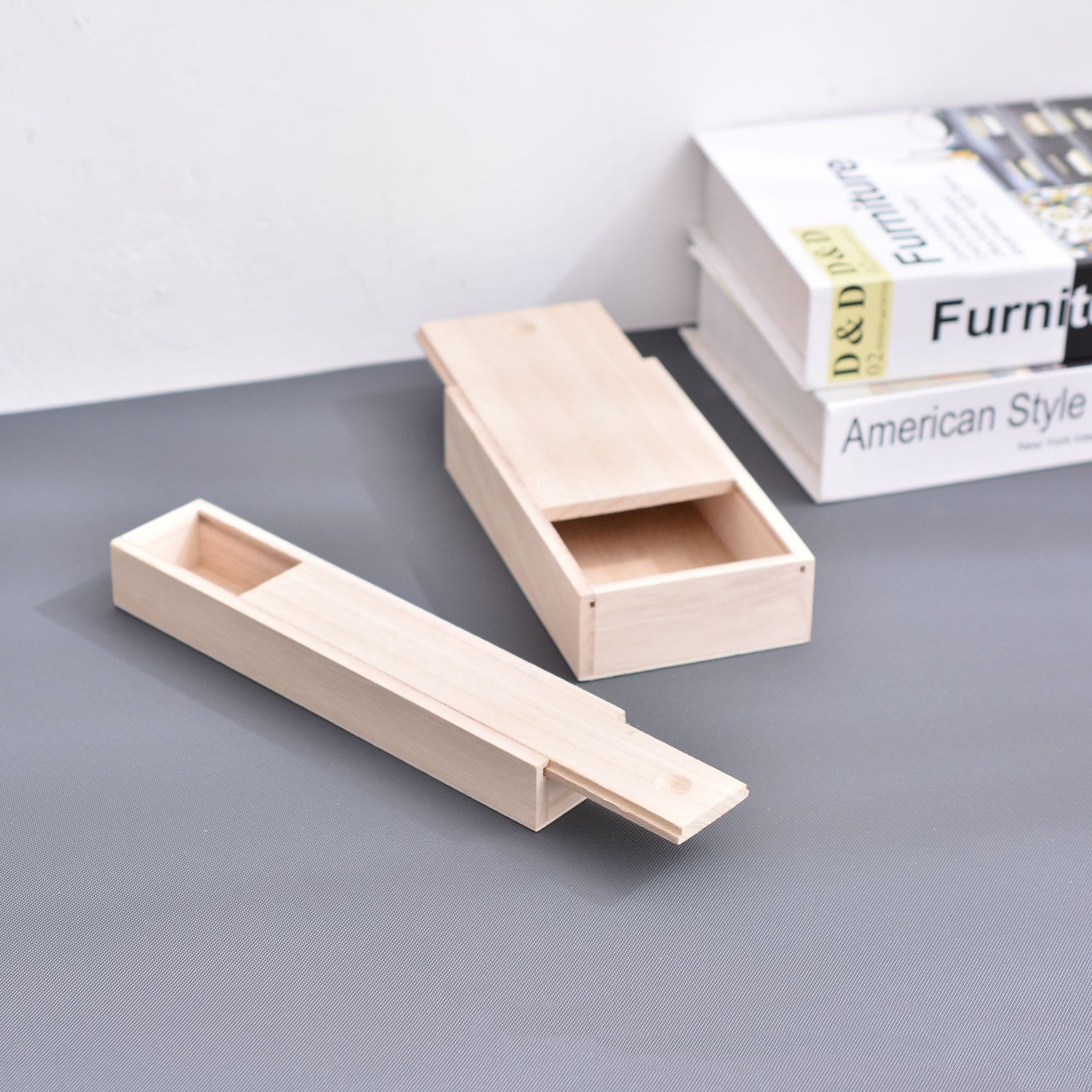 Light wood box with sliding lid, open, resting on a gray surface. Book is in background.