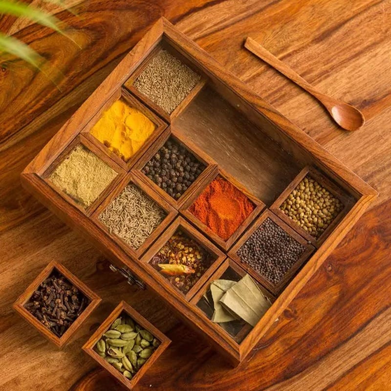Wooden spice box with compartments filled with colorful spices and a small wooden spoon.